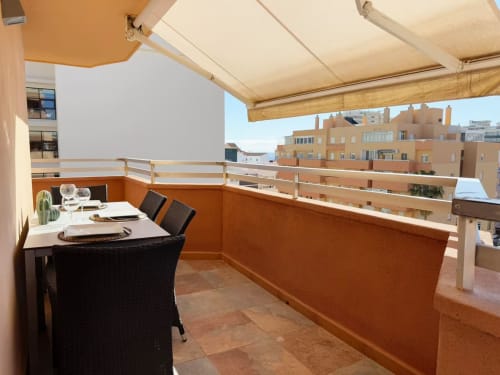 Balcón moderno de apartamento frente al mar en Fuengirola con zona de comedor, toldo retráctil y vistas a la ciudad