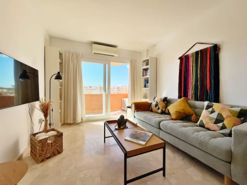 Moderno apartamento frente al mar en Fuengirola con sofá gris, cojines coloridos, balcón con vistas a la ciudad y diseño contemporáneo