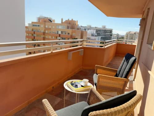 Soleado balcón moderno en Fuengirola con vistas a la ciudad, muebles de mimbre y paredes terracota naranjas con vista panorámica