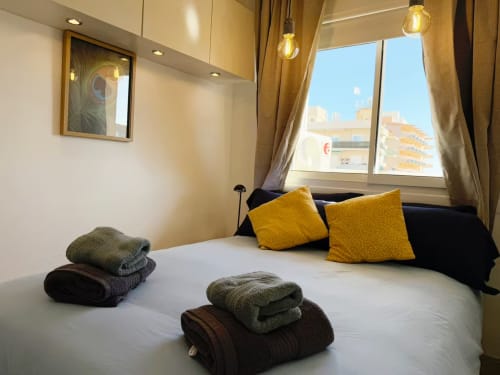 Moderno apartamento frente al mar en Fuengirola con vistas a la ciudad, cama blanca, almohadas doradas y toallas dobladas