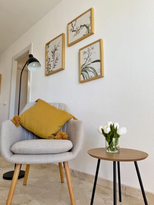 Moderno apartamento soleado en Fuengirola con sillón beige, almohada mostaza, lámpara arco y arte botánico en pared