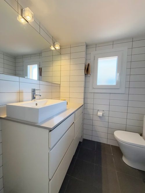 Baño moderno con lavamanos blanco, paredes alicatadas, inodoro y ventana en apartamento de playa soleado, Fuengirola