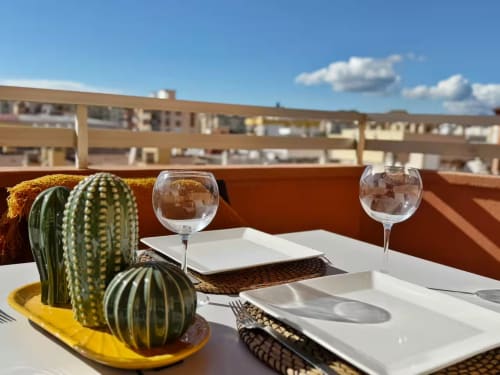 Terraza soleada para comer en Fuengirola con cactus, copas de vino y vistas de la ciudad con edificio moderno