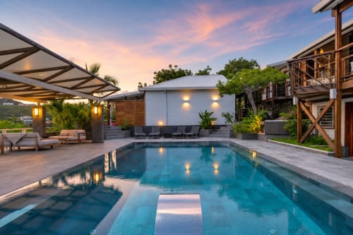Vue coucher de soleil de la villa Les Balcons D'oyster Pond avec piscine illuminée, bains de soleil et vue sur la mer des Caraïbes à Saint-Martin