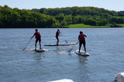 Quatre personnes en paddle sur le lac de Valjoly près de Solre-le-Château, forêts vertes et prairies en arrière-plan