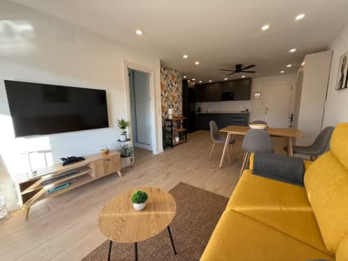 Moderno y luminoso salón de apartamento en Fuengirola con sofá amarillo, muebles de madera y cocina abierta