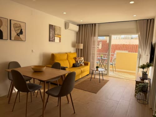 Elegante apartamento soleado en Fuengirola con sofá amarillo, mesa de comedor y terraza con vistas a tejados de barro rojo