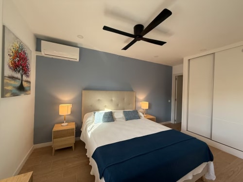 Dormitorio moderno en apartamento de Fuengirola con pared azul, ventilador de techo y mobiliario elegante