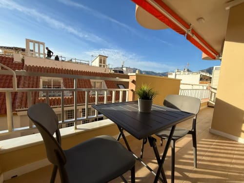 Terraza soleada con mesa de comedor vista a Fuengirola, montañas, toldo rojo y apartamento beige