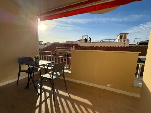 Terraza soleada con asientos con vista a los tejados de Fuengirola, toldo rojo, vista de apartamento frente al mar
