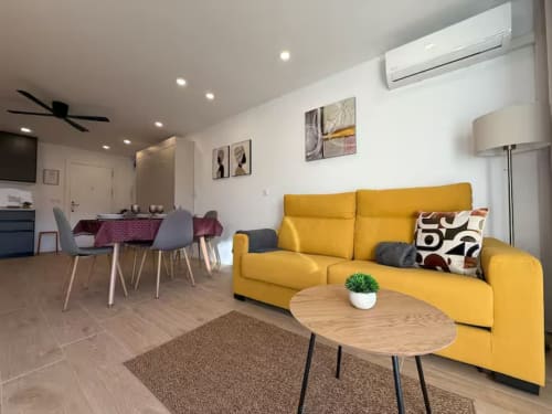 Elegante apartamento de playa con luz natural en Fuengirola, sofá amarillo, mesa de madera y mobiliario moderno