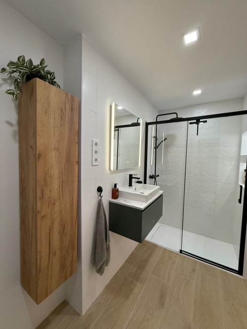 Baño moderno con detalles en madera, accesorios negros y mamparas de cristal en apartamento de Grupo Inmohouse en Fuengirola