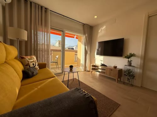 Moderno apartamento soleado en Fuengirola con sofá amarillo, TV de pantalla plana y balcón con vistas a la ciudad
