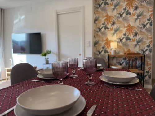 Mesa de comedor elegante para cuatro con vajilla crema y mantel estampado burdeos en apartamento playa de Fuengirola