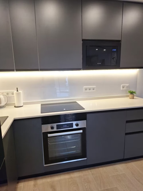 Cocina moderna en apartamento de playa en Fuengirola con luz natural, armarios grises, encimeras blancas y electrodomésticos de acero inoxidable