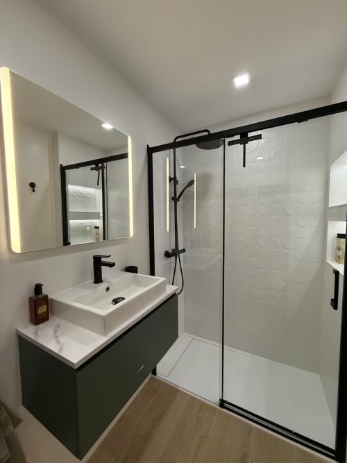 Baño moderno en soleado apartamento de playa en Fuengirola con accesorios negros, espejo LED y ducha abierta