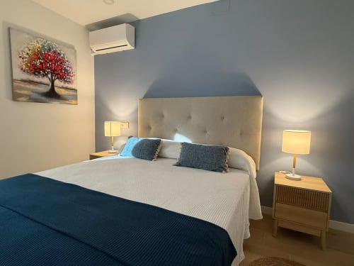 Elegante habitación de apartamento frente al mar en Fuengirola con cabecero neutro, acentos azules, camas gemelas, lámparas y diseño moderno