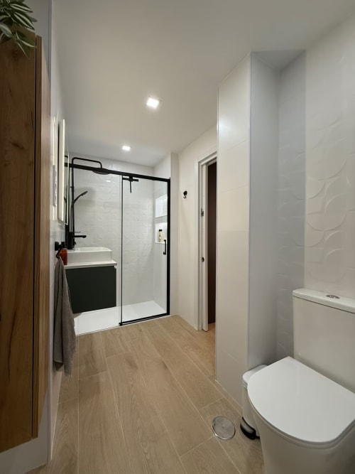 Baño moderno en elegante apartamento de playa en Fuengirola con ducha de cristal, accesorios negros y suelos de madera