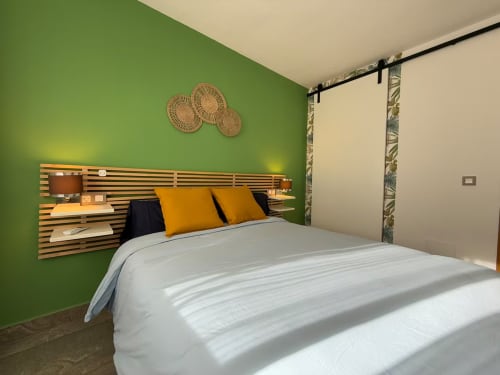 Dormitorio luminoso en apartamento de playa moderna en Fuengirola con paredes verdes, cabecero de madera y almohadas doradas
