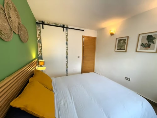 Dormitorio moderno y soleado de apartamento playa en Fuengirola con cabecero amarillo, pared de acento verde y decoración contemporánea