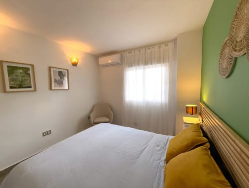 Soleado dormitorio de apartamento en playa en Fuengirola con pared de acento verde, cama doble y vistas a la ciudad