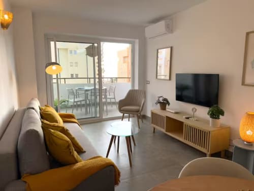 Moderno apartamento soleado en Fuengirola con vistas a la ciudad, sala de estar contemporánea, acentos amarillos, acceso a balcón