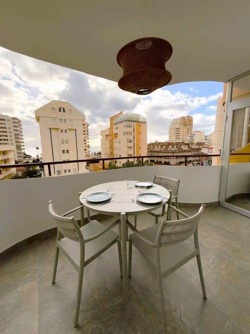 Balcón moderno y soleado de apartamento en la playa de Fuengirola con mesa de comedor con vistas a los edificios de la ciudad