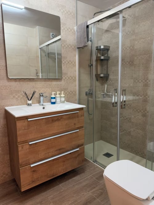 Moderno baño soleado en apartamento frente al mar en Fuengirola con tocador de madera, ducha de cristal y azulejos contemporáneos