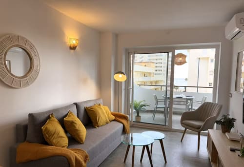 Moderno apartamento soleado en Fuengirola con sofá gris, detalles amarillos y vistas de la ciudad desde el balcón