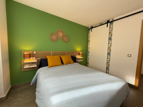 Dormitorio moderno en apartamento de playa soleado en Fuengirola con pared acentuada en verde, cabecera de madera y almohadas amarillas