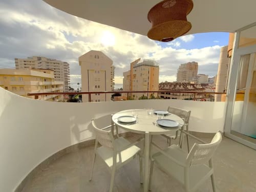 Balcón moderno y soleado de apartamento frente al mar en Fuengirola con vistas a la ciudad, mesa de comedor y edificios costeros