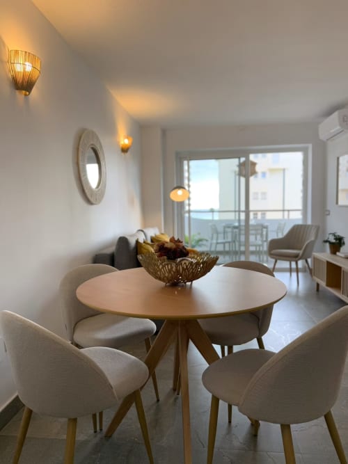 Luminosa zona de comedor en apartamento costero de Fuengirola con mesa redonda, sillas neutras y vistas a la ciudad