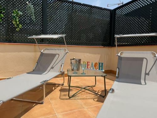 Terraza frente al mar soleada en Grupo Inmohouse, apartamento en Fuengirola con tumbonas, mesita y colorido cartel 'BEACH'