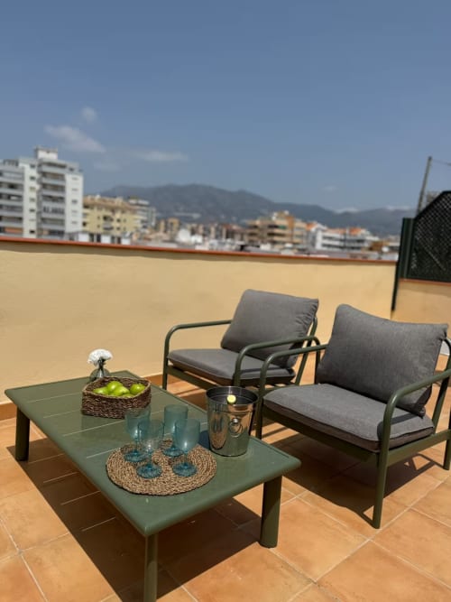 Soleada terraza en azotea de Fuengirola con tumbonas verdes, mesa de café y vistas a las montañas
