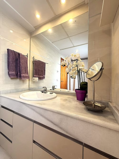 Baño moderno con encimera de mármol, lavabo redondo y orquídea blanca en apartamento de playa en Fuengirola
