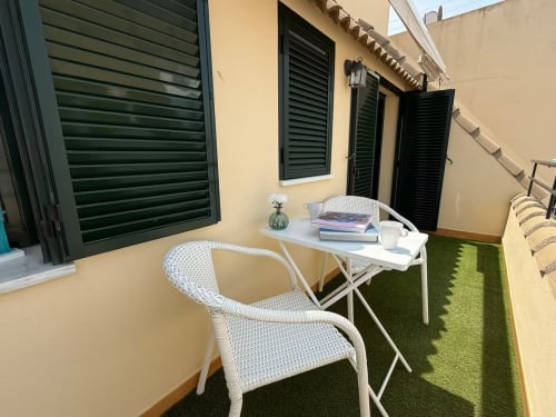 Terraza soleada de apartamento frente al mar en Fuengirola con silla de mimbre blanca, mesa y césped artificial