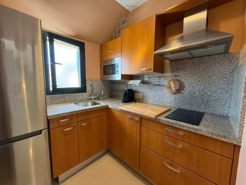 Cocina moderna con muebles de madera, encimeras de granito y electrodomésticos de acero inoxidable en apartamento frente al mar en Fuengirola