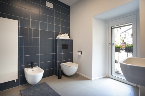 Bagno moderno a Camere d'Aria a Locana con pareti in piastrelle scure, sanitari bianchi e porta in vetro verso il balcone
