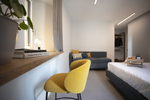 Camera moderna presso Camere d'Aria BnB a Locana con poltrona gialla, scrivania, divano scuro e letto bianco