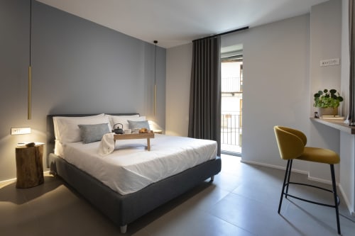 Camera moderna presso Camere d'Aria a Locana con letto matrimoniale, poltrona color senape, balcone e vista sulla città