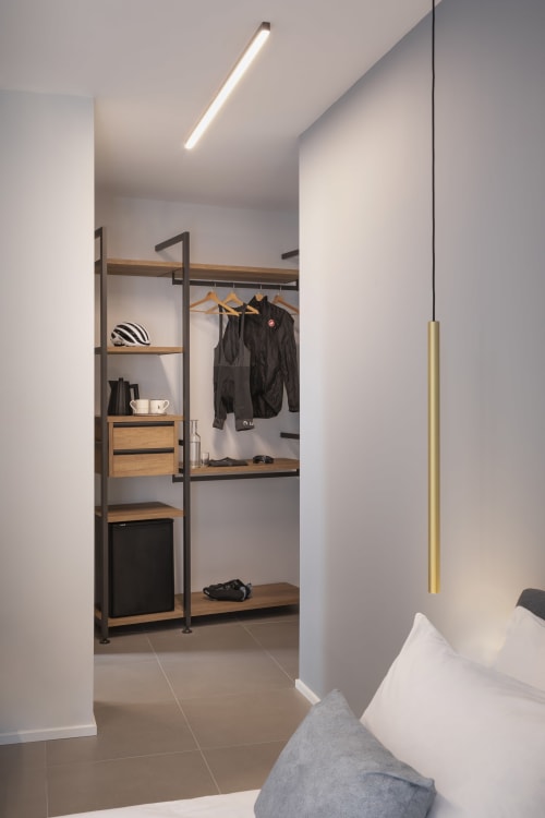 Elegante guardaroba in camera da letto con scaffali in legno, abiti neri appesi e illuminazione a sospensione presso Camere d'Aria B&B a Locana