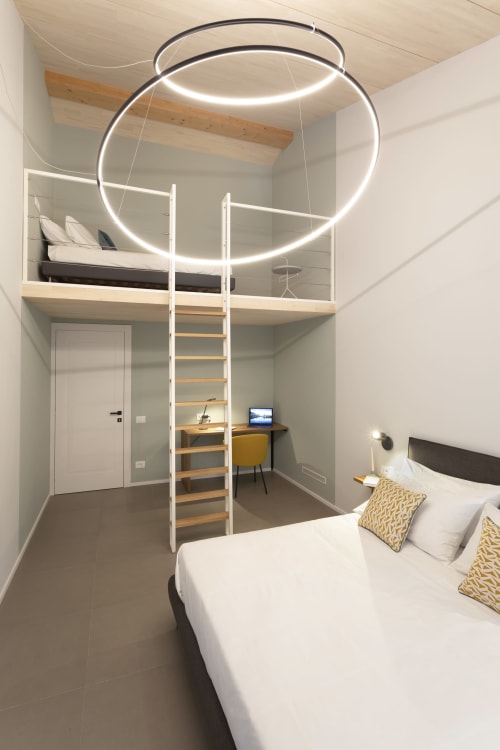 Camera da letto in loft moderno con anello di luce neon, letto in mezzanino, zona studio e scala bianca presso l'hotel boutique Camere d'Aria