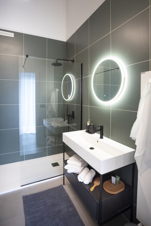 Bagno moderno a Camere d'Aria a Locana con specchi LED, lavabo bianco, pareti piastrellate scure e cabina doccia in vetro