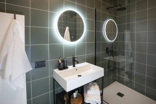 Bagno moderno presso Camere d'Aria BnB a Locana con specchi illuminati, lavabo bianco, rubinetteria nera e piastrelle verdi