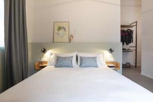 Modern double bedroom at Camere d'Aria in Locana with white bed, blue pillows, wooden nightstands, and mountain view access