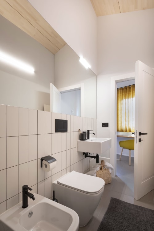 Modern bathroom at Camere d'Aria in Locana with white tiles, toilet, bidet, sink, and open doorway to bedroom
