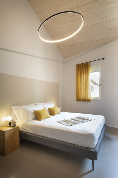 Modern bedroom at Camere d'Aria with queen bed, yellow accents, pendant light, and mountain views in Locana