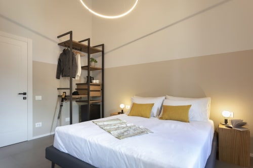 Modern double bedroom at Camere d'Aria in Locana with white bedding, mustard pillows, wooden nightstand, and metal clothing
