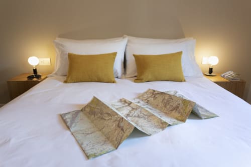 Cozy double bedroom at Camere d'Aria B&B in Locana with white linens, gold cushions, and travel maps on bed
