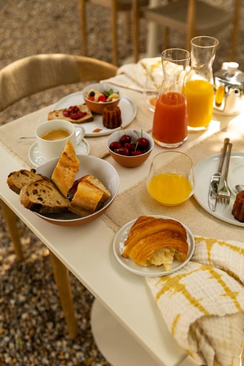 Table de petit-déjeuner à la Maison Girardine avec croissants, café, fruits frais, jus d'orange et pain à Rauzan